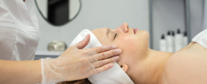 Woman receiving a facial treatment while lying down, with a therapist gently touching her face wearing gloves.